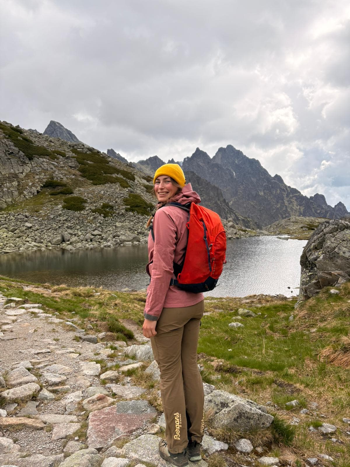 Kristína standing by a mountain tarn beneath jagged peaks