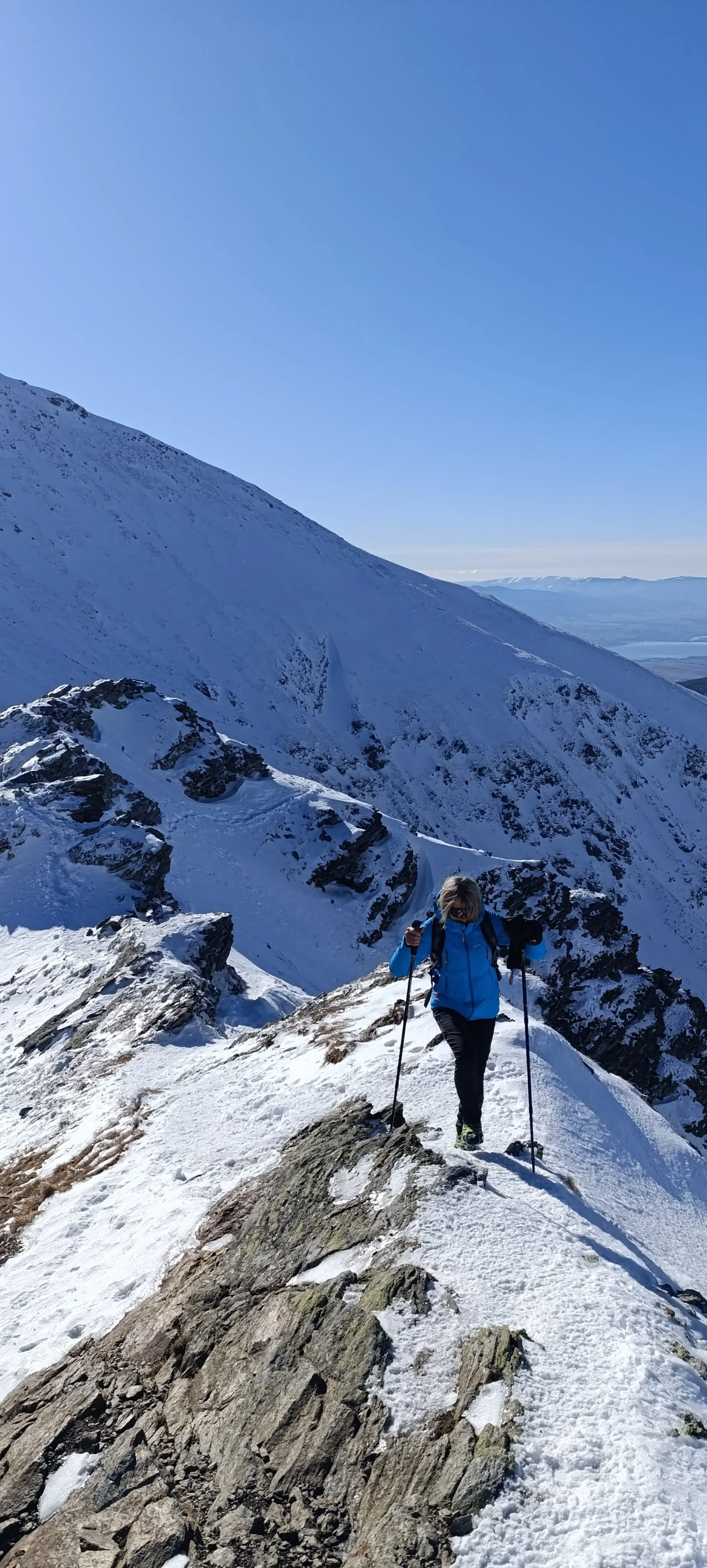 A walker climbing a snow-covered ridge under a clear winter sky